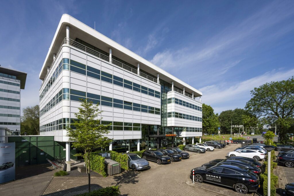 Modern kantoorgebouw aan de Burgemeester Stramanweg met geparkeerde auto's op de voorgrond.